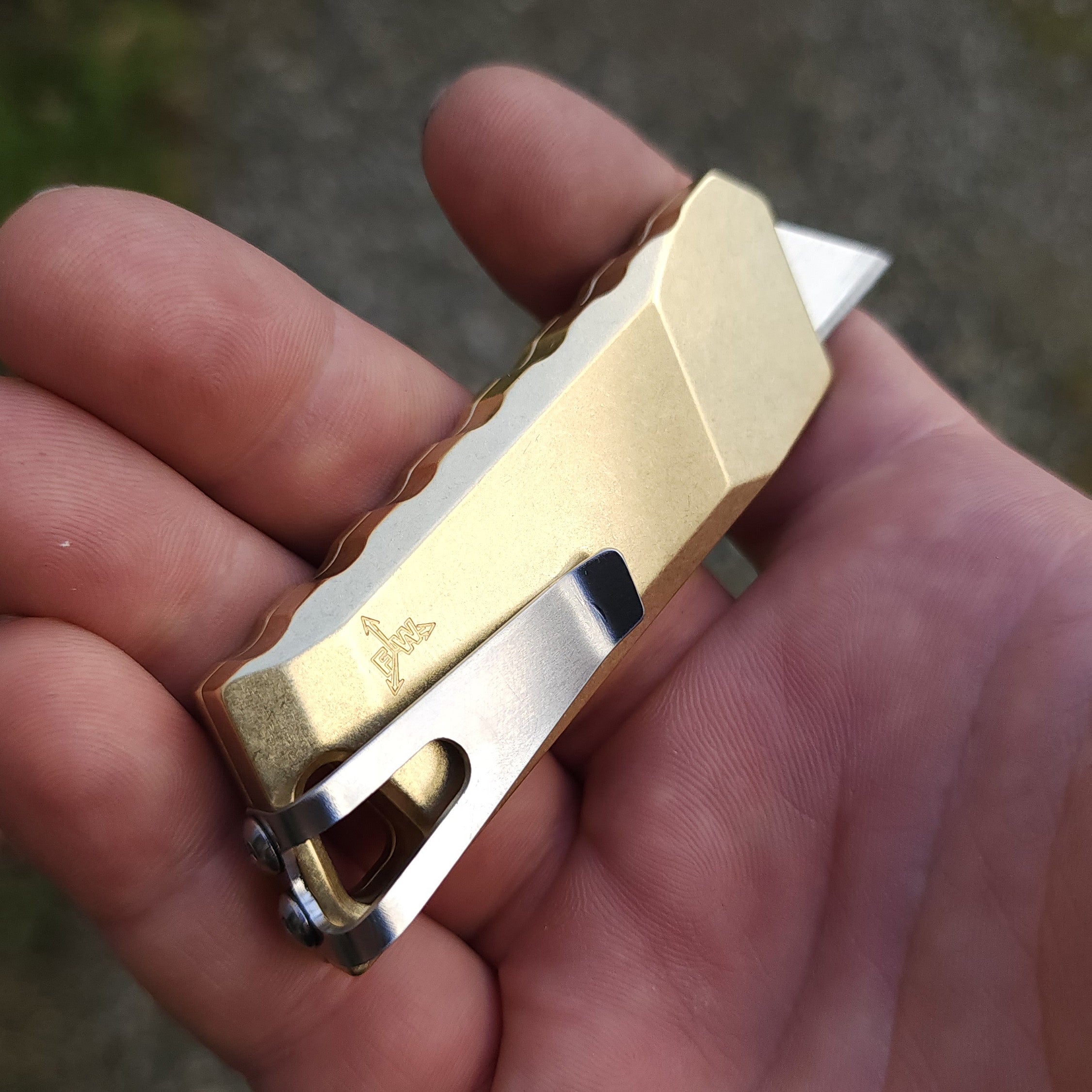 backside of focusworks bob the boxcutter in brass with pocket clip in someones hand